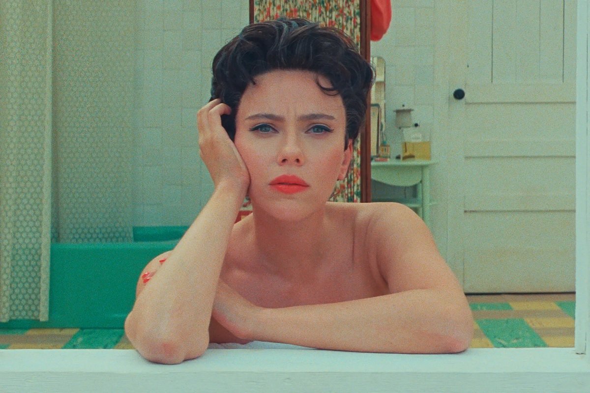 Scarlett Johansson stares out a motel window at the camera in Asteroid City.