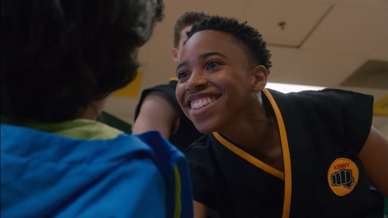 An image from Cobra Kai season four shows Kenny Payne smiling over Anthony Russo