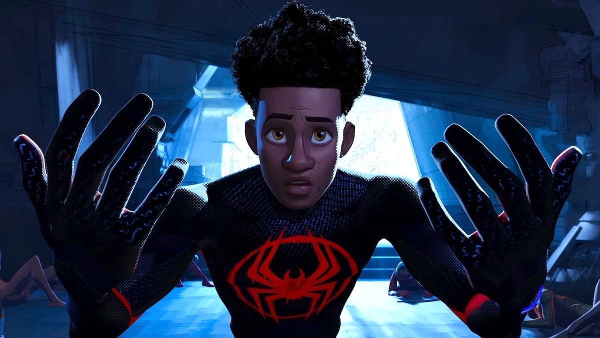 Miles Morales in his black and red Spider-Man suit holds his hands up in front of his unmasked face in Across the Spider-Verse