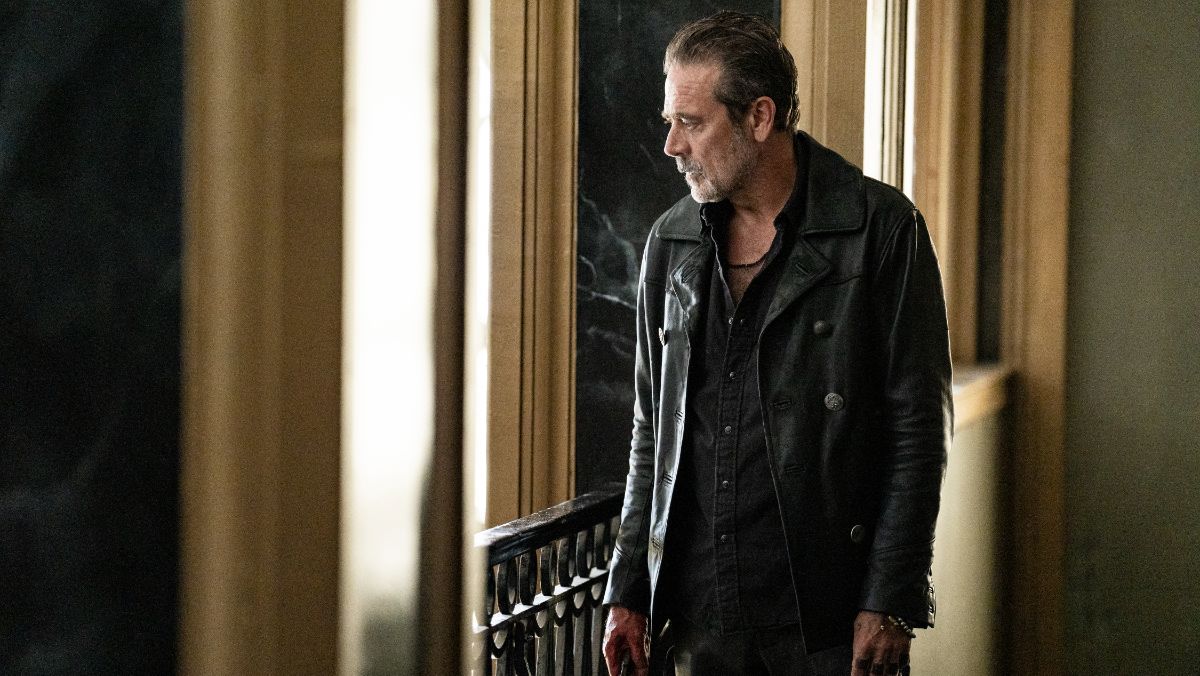 Negan looks out of a window while wearing leather jacket